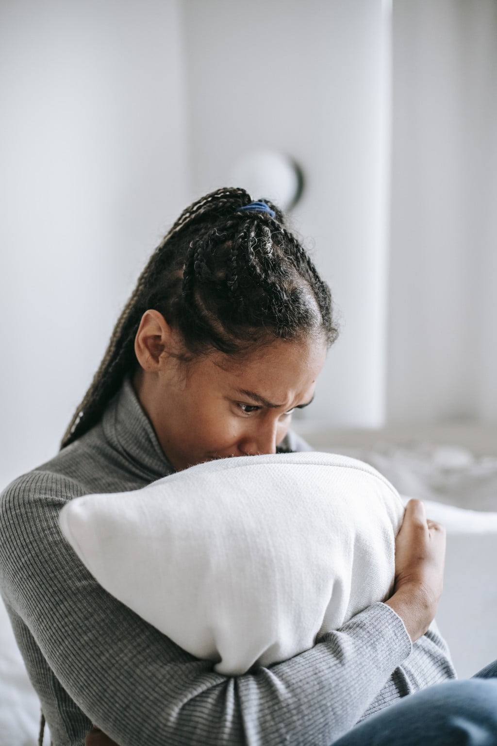 Crying black woman hugging pillow in bedroom